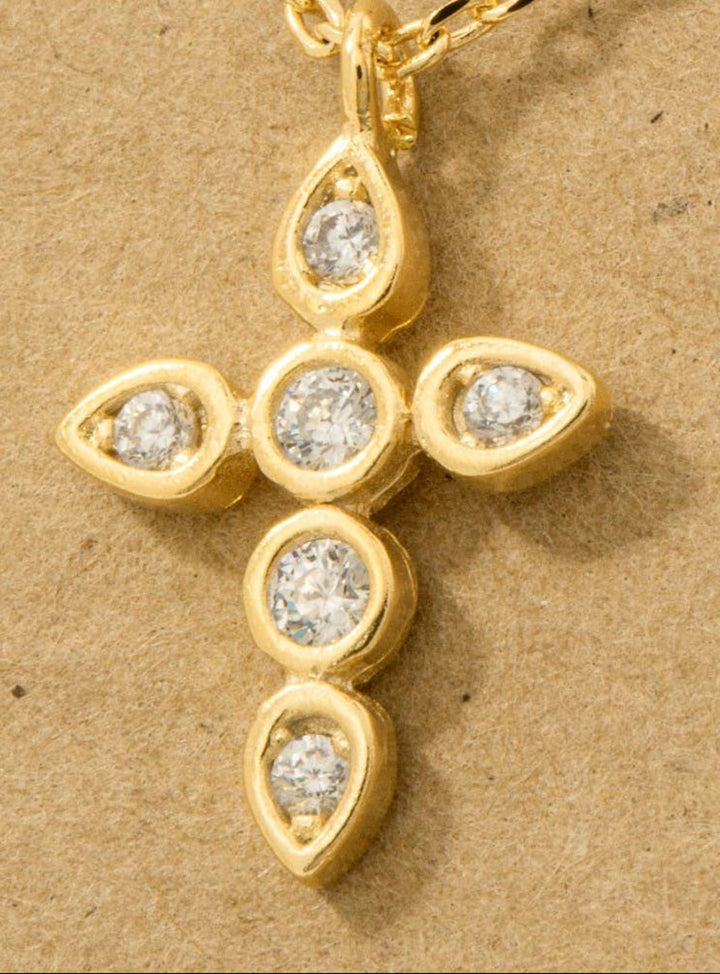 Gold cross pendant with embedded cubic zirconias on a beige background