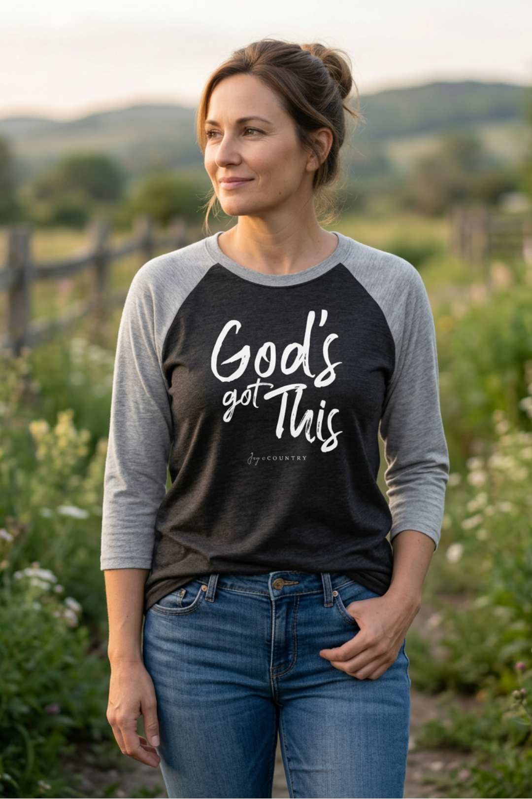Woman wearing a black and gray baseball shirt with 'God's got this' text in a field.