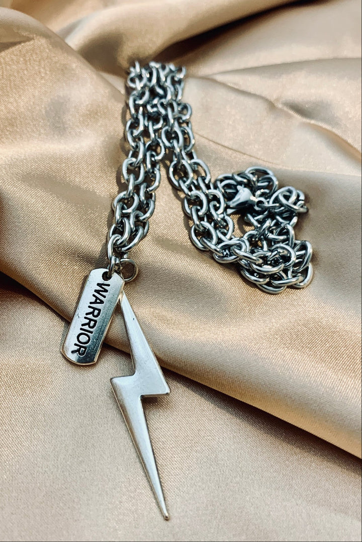 Silver chain necklace with a lightning bolt and warrior charms on beige fabric