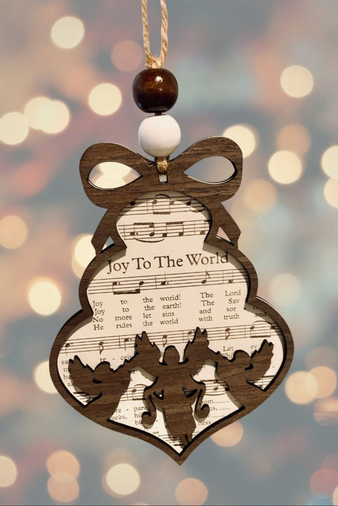 Decorative Christmas ornament with sheet music design and 'Joy To The World' text, against a blurred festive background.
