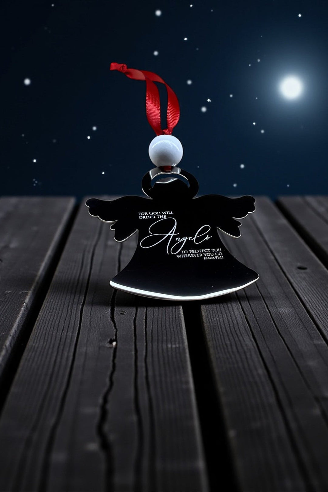 Stainless steel angel ornament with red ribbon on a wooden surface at night