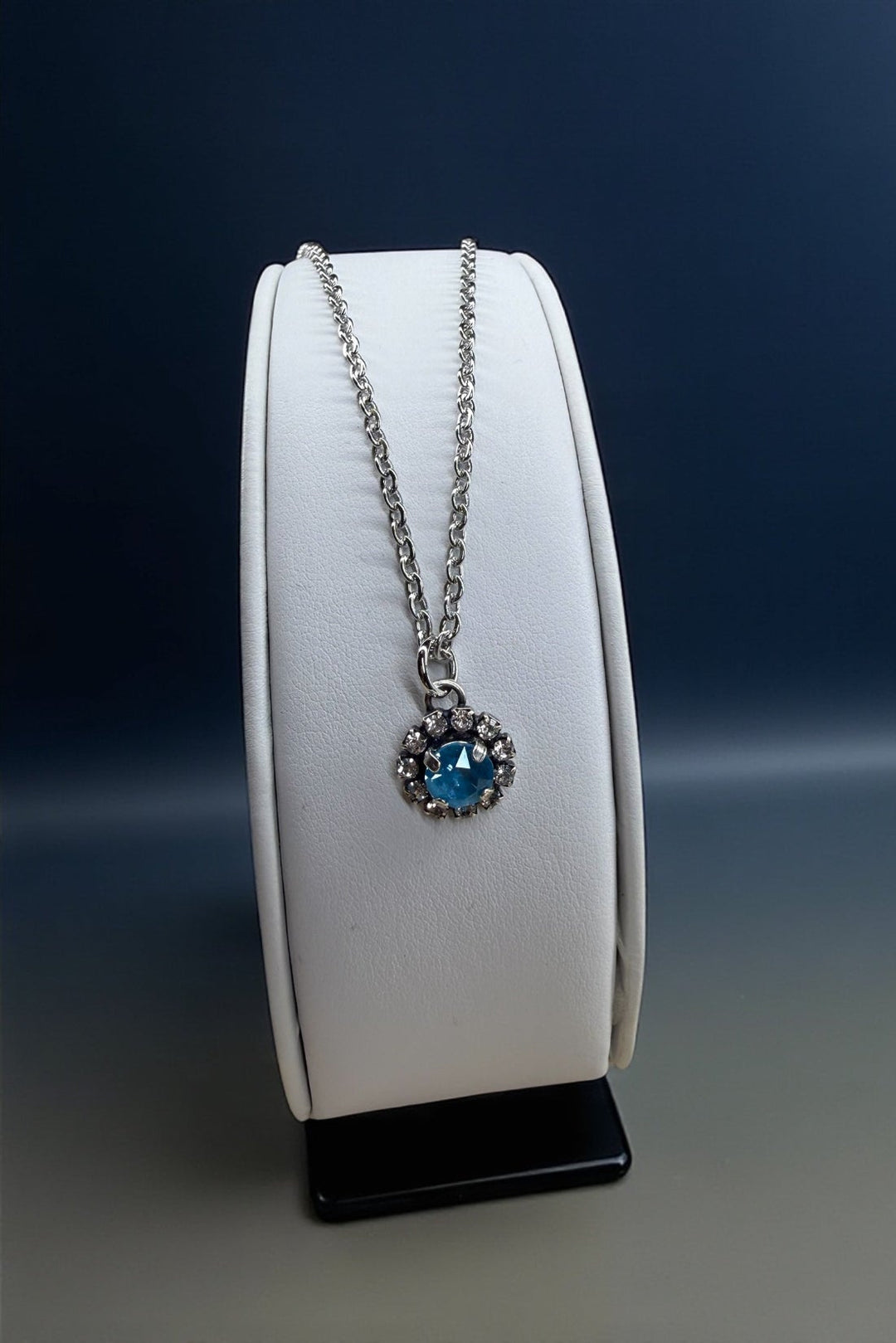 Necklace with a blue crystal on a white stand against a dark background