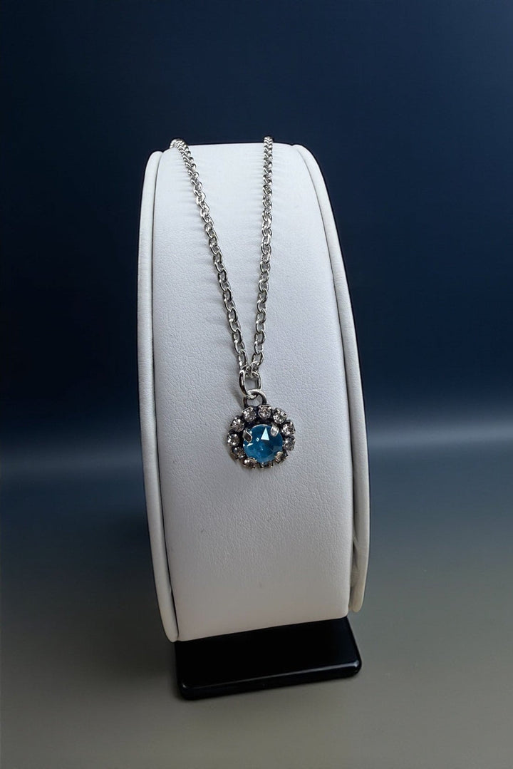 Necklace with a blue crystal on a white stand against a dark background
