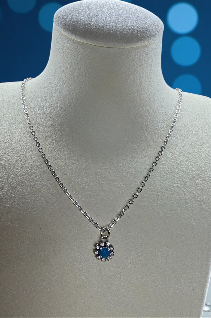 Silver necklace with a blue opal crystal pendant surrounded by rhinestones on a mannequin bust against a blue blurred background