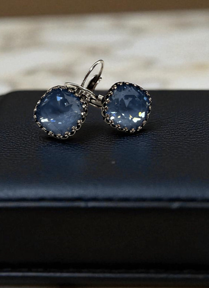 Pair of blue gemstone earrings on a black jewelry box with a marble background