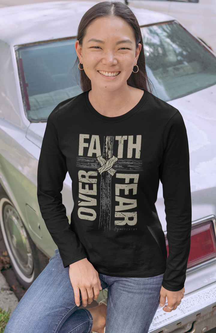 Person wearing a black long-sleeve shirt with 'Faith Over Fear' text and cross graphic, sitting in front of a vintage car.